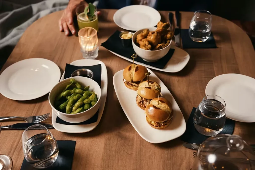 Top-down: Warmly lit dining table with appetizers, drinks, and lit candle.