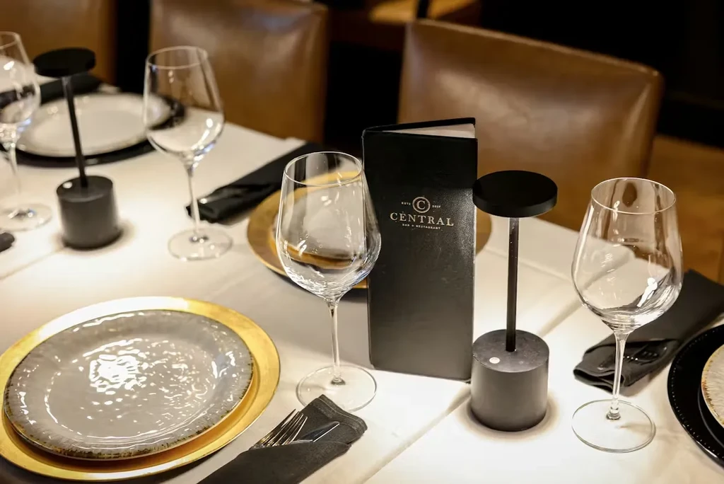 Restaurant table set with gold-rimmed plates, cutlery, lamps, and C CENTRAL menu.