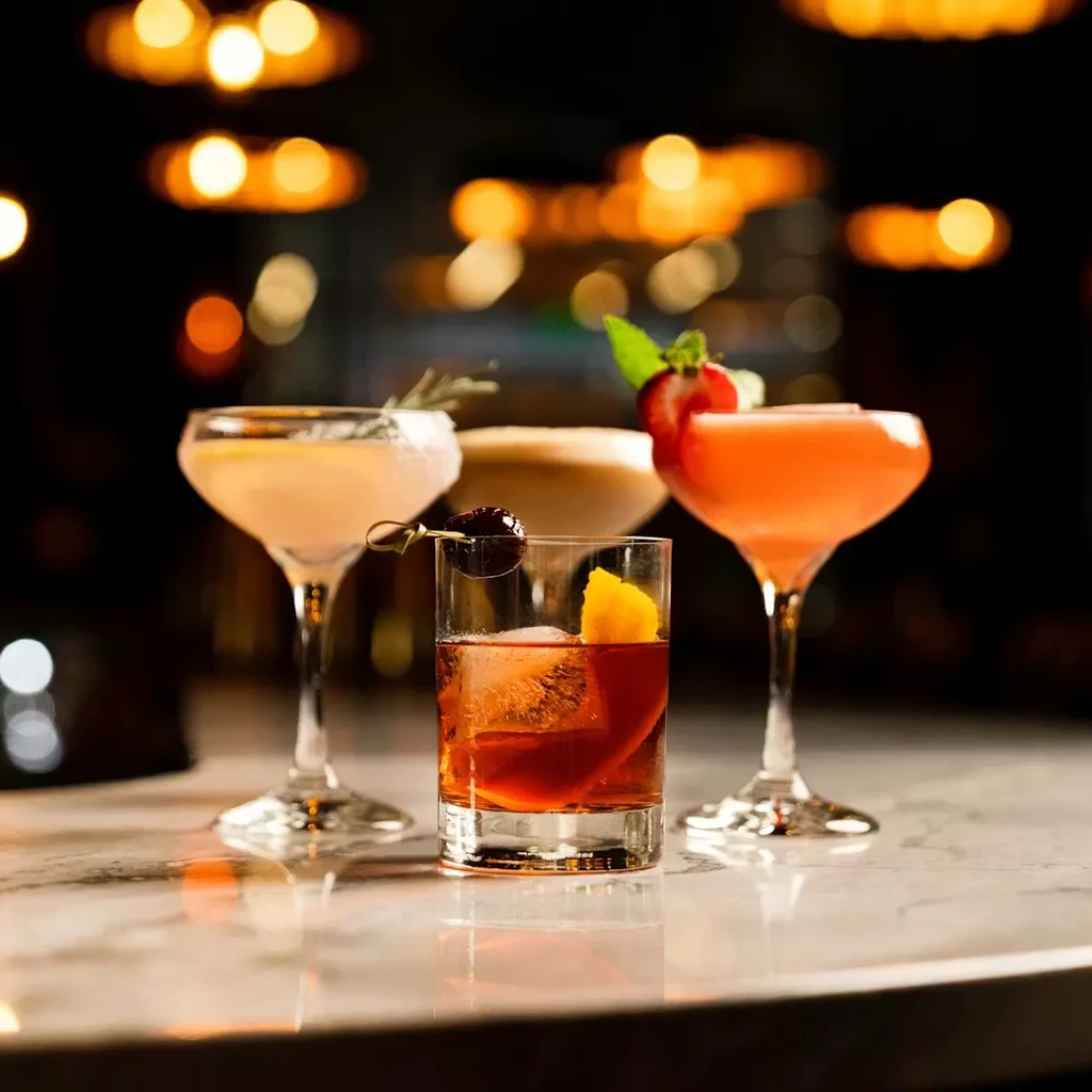 Four diverse cocktails on a reflective counter with a blurred light background.