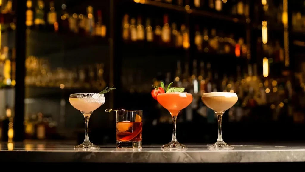 Four distinct cocktails with garnishes on a dimly lit bar.