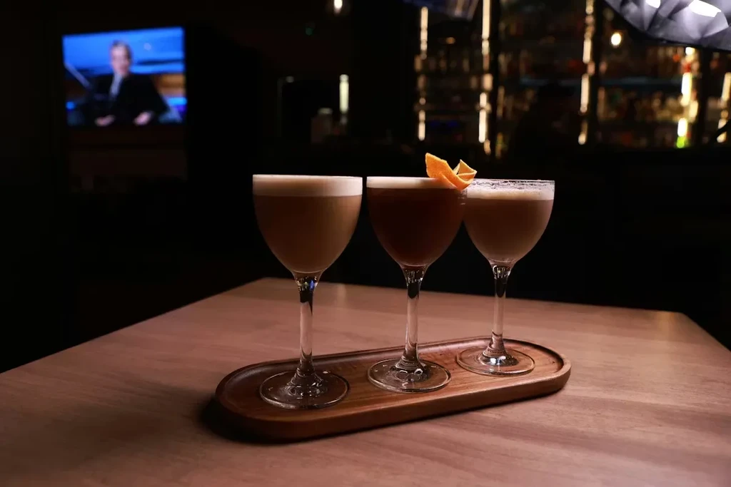 Three elegant cocktails with foamy tops on a dark wooden tray.