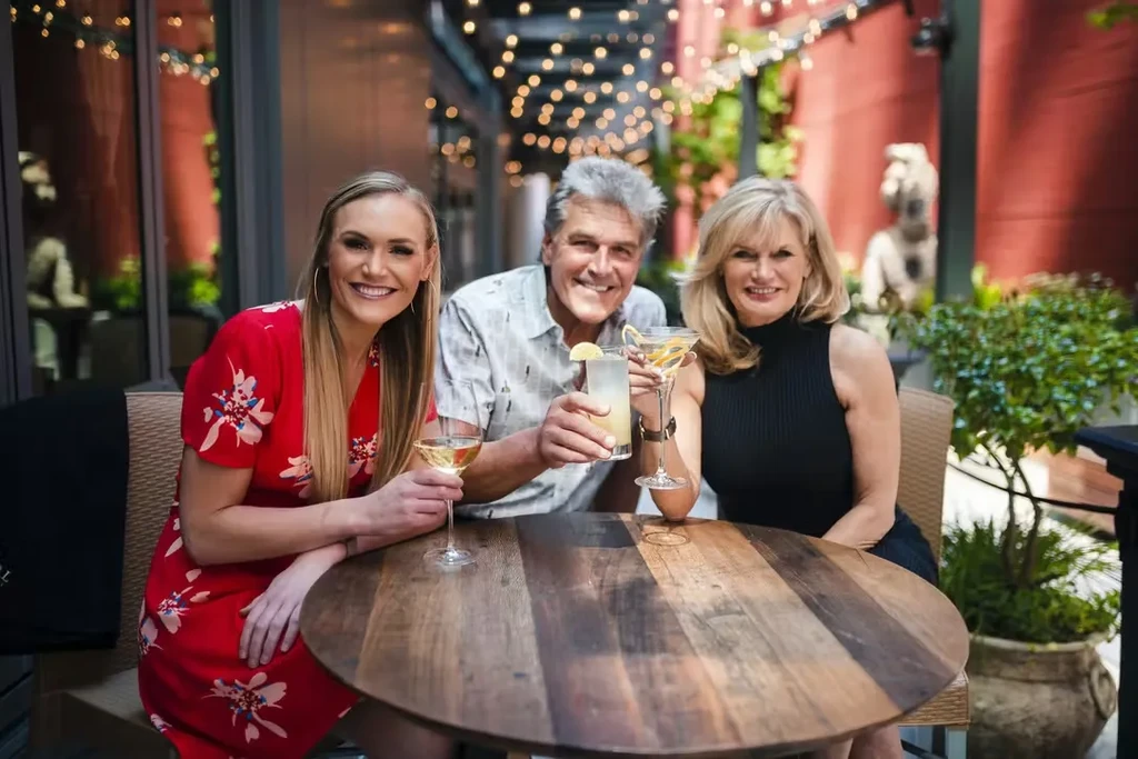 Three smiling people holding drinks on an outdoor patio.