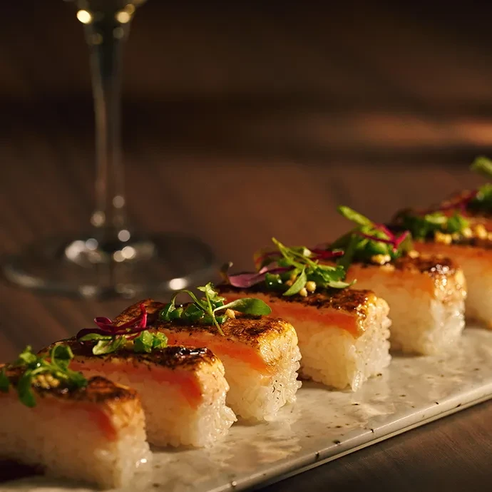 Six pieces of seared salmon nigiri with microgreens on a plate.
