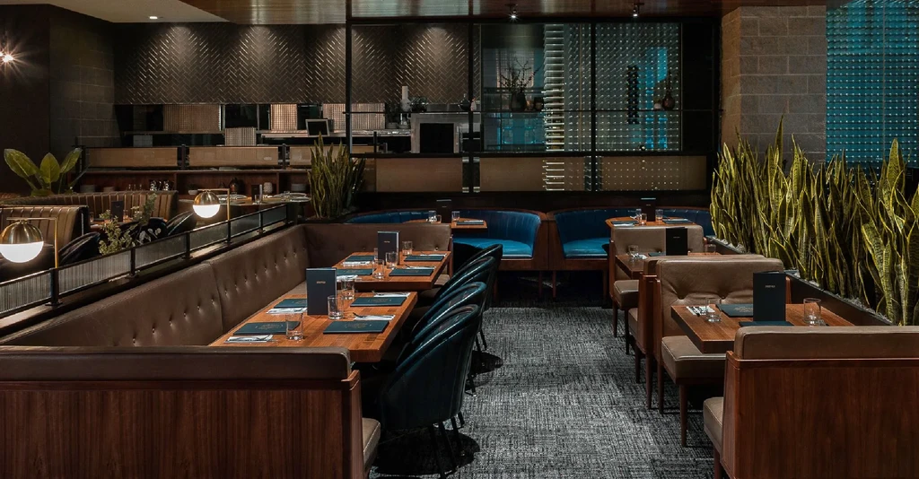 Empty upscale restaurant with dark leather seating, pendant lights, and plants.