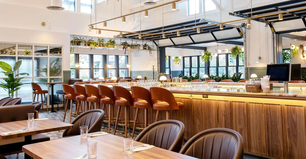 Modern restaurant interior with wooden tables, a marble bar, and plants.