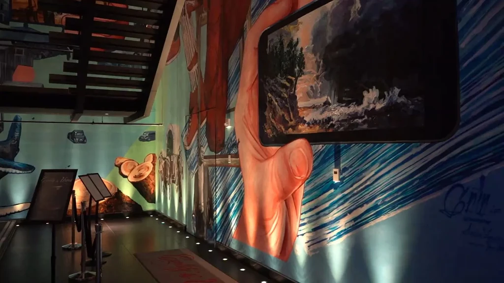 Interior hallway with vibrant murals, stairs, and a hand holding a smartphone.