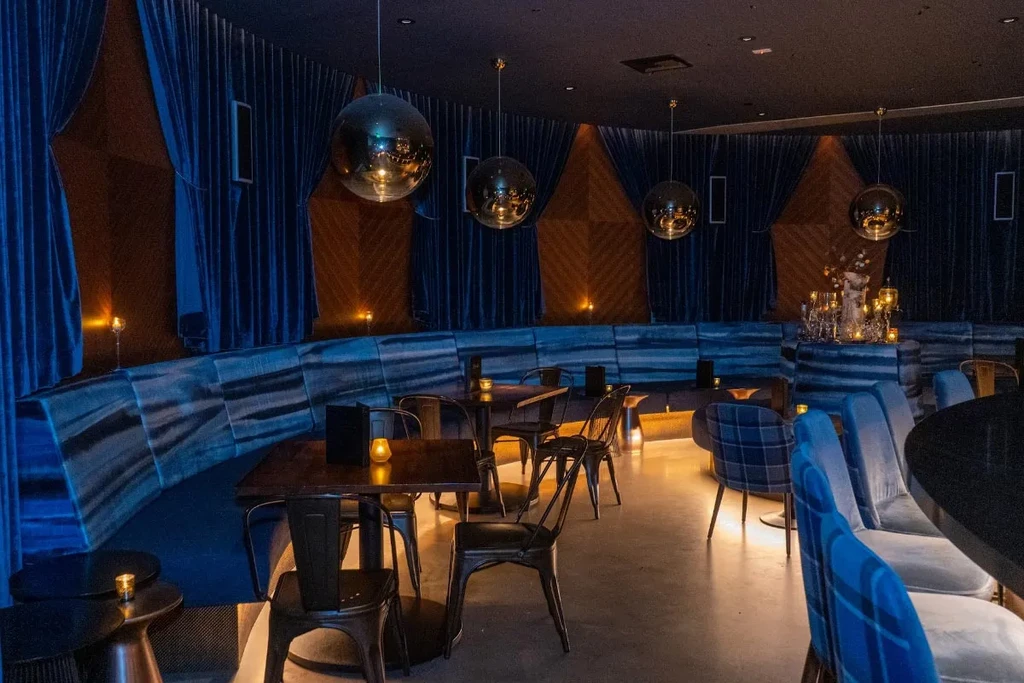 Dimly lit bar interior: blue velvet, wood, disco balls, candles.