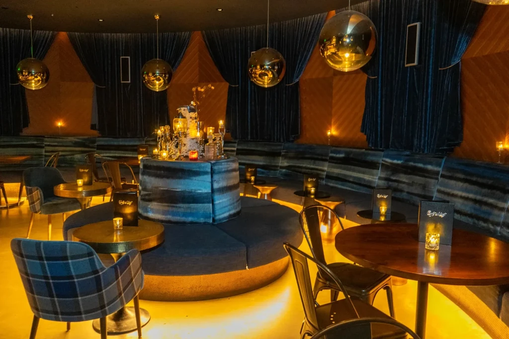 Sophisticated, dimly lit bar with circular seating and hanging spherical lights.