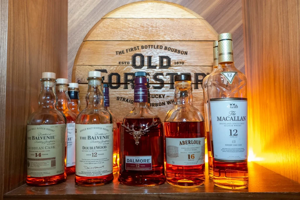 Whisky bottles arranged on a wooden shelf with an Old Forester barrel.