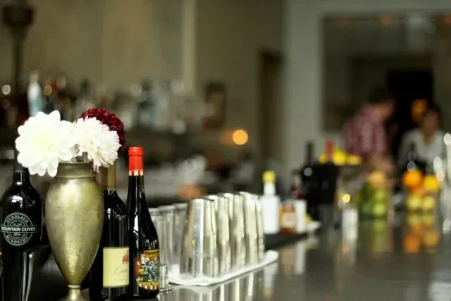 Refined bar counter with flowers, wine bottles, cocktail shakers, and blurred staff.