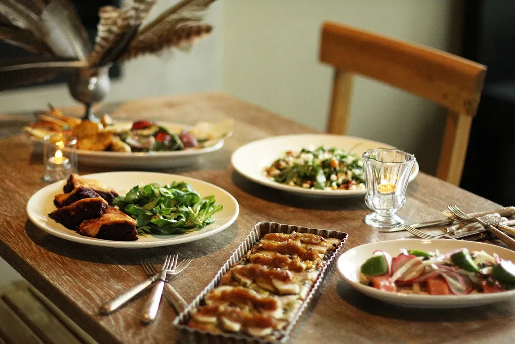 Dining table with savory tarts, sliced fish, salads, and a lit candle.