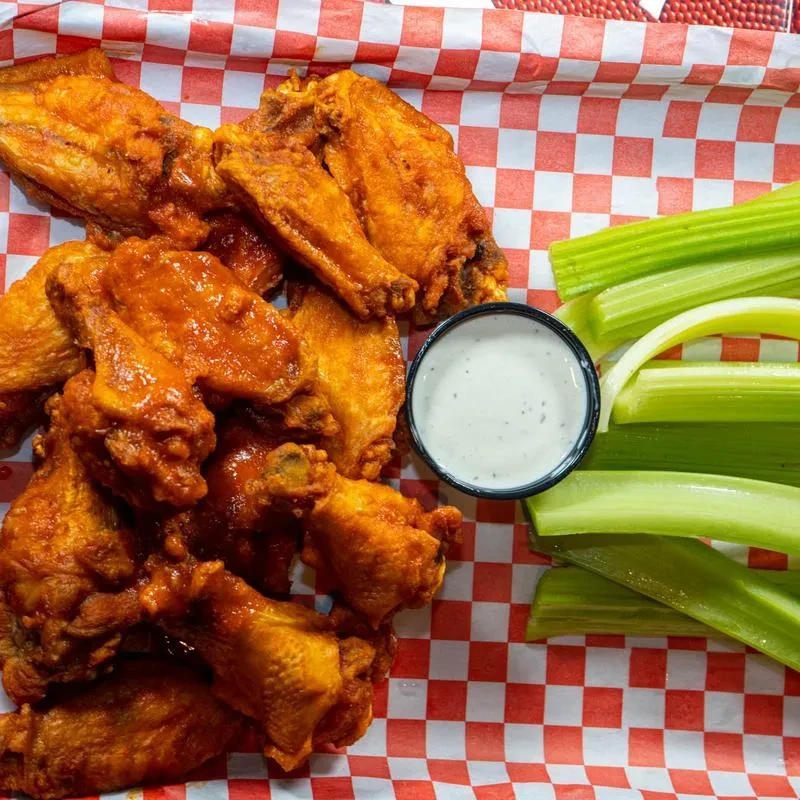 Glossy buffalo chicken wings, celery, and dip on a checkered liner.