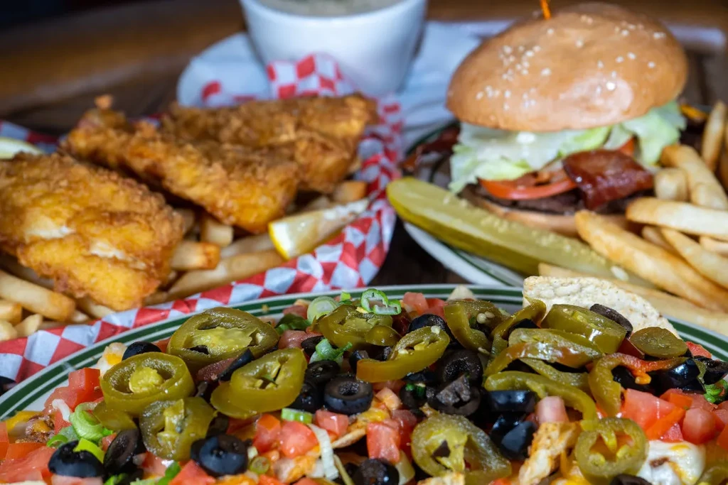 Close-up of nachos, fried fish, burger, and fries on a wooden table.