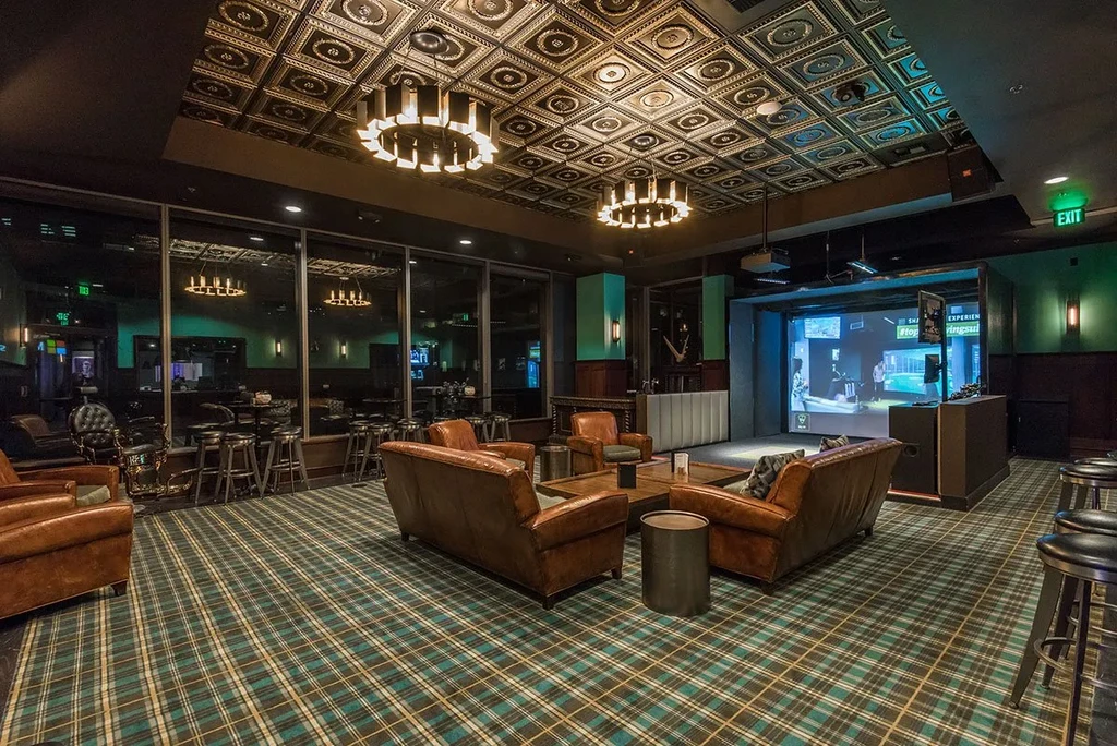 Lounge with pressed metal ceiling, plaid carpet, and golf simulator.