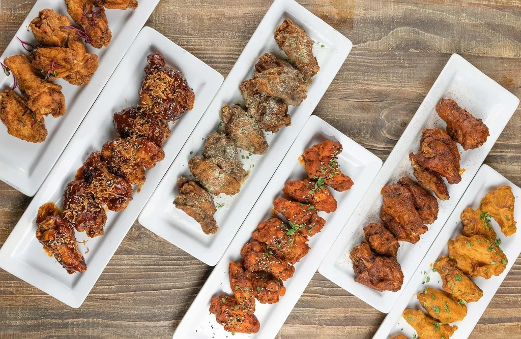 Overhead view of six plates of assorted chicken wings on a table.