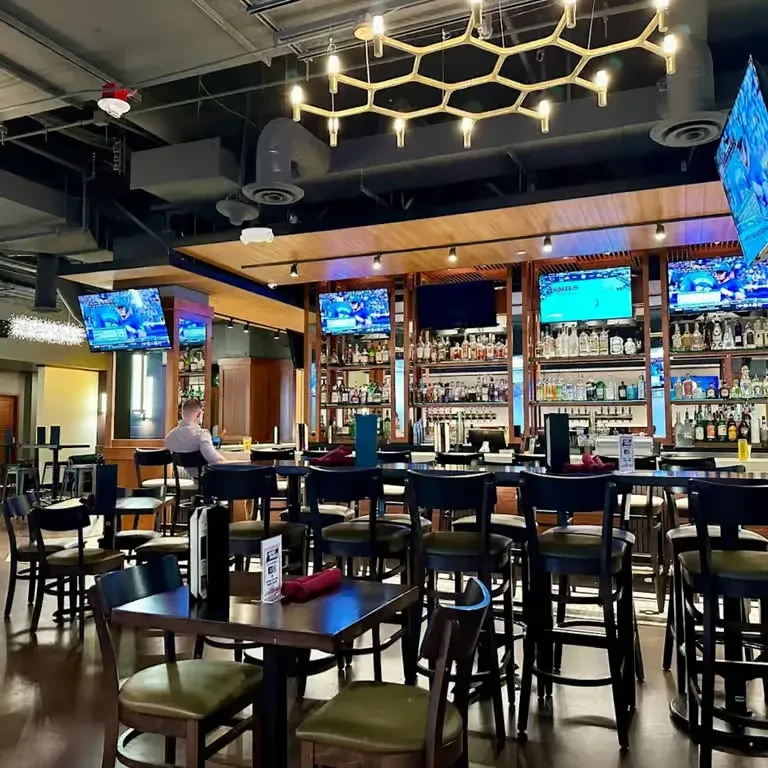 Modern bar interior featuring a stocked bar, sports TVs, and seating.