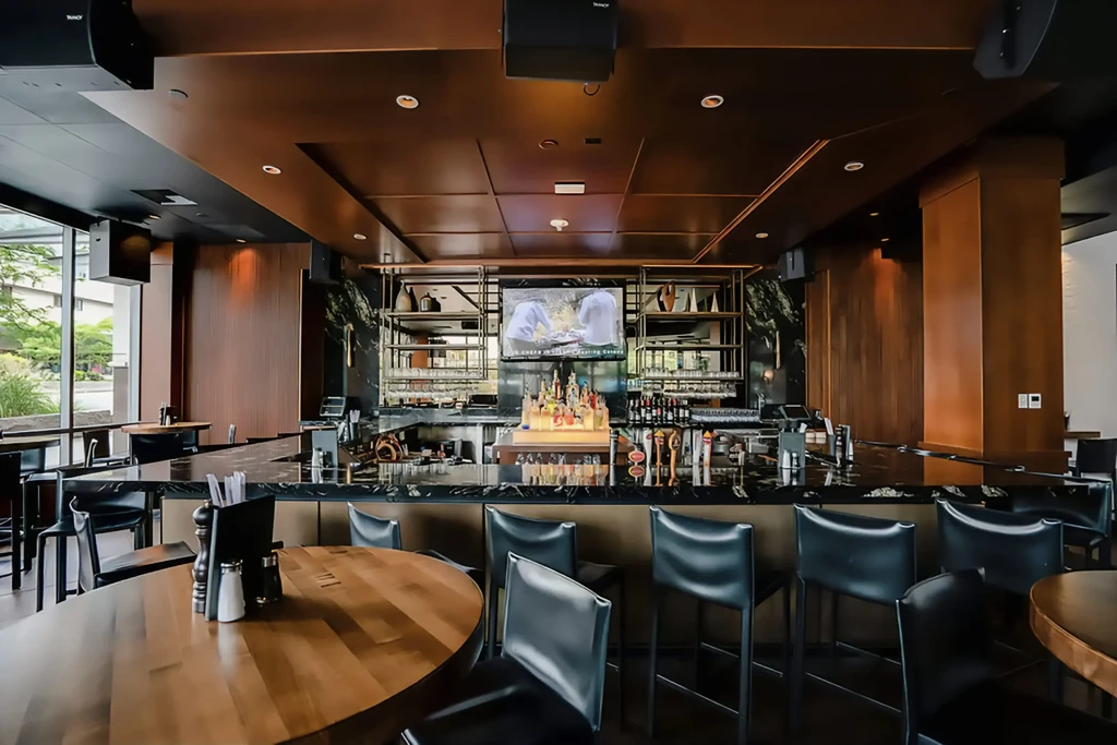 Well-stocked modern bar with dark counter, stools, and a TV.