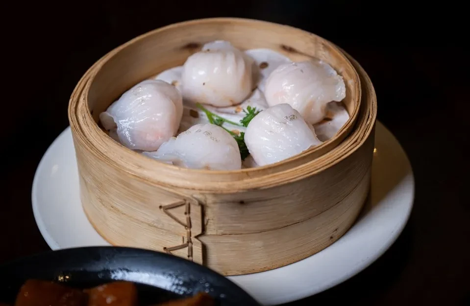 Five translucent white dumplings in a bamboo steamer with green garnish.