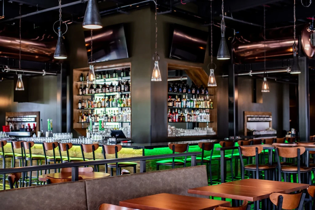 Well-stocked bar with vibrant green underglow and exposed industrial ceiling.