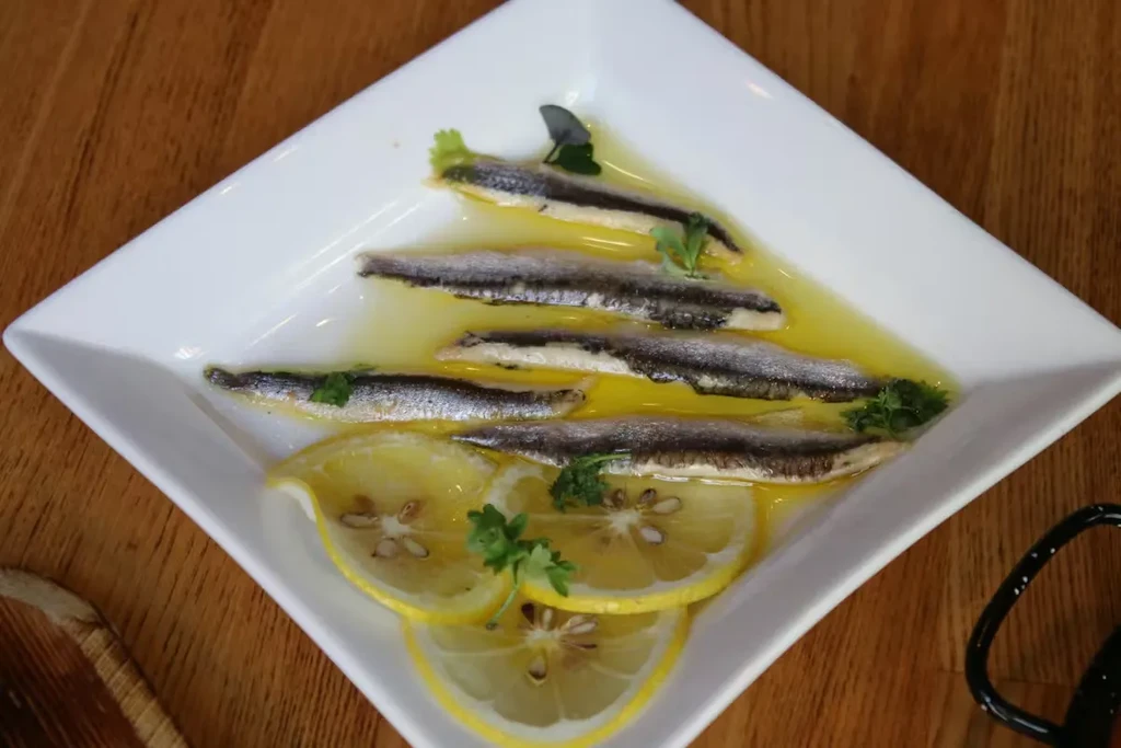 Marinated anchovies in olive oil with lemon and herbs on white plate.