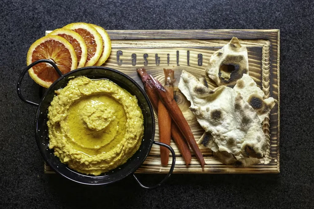 Creamy dip, charred flatbread, and dried oranges on a rustic "Castilla" board.