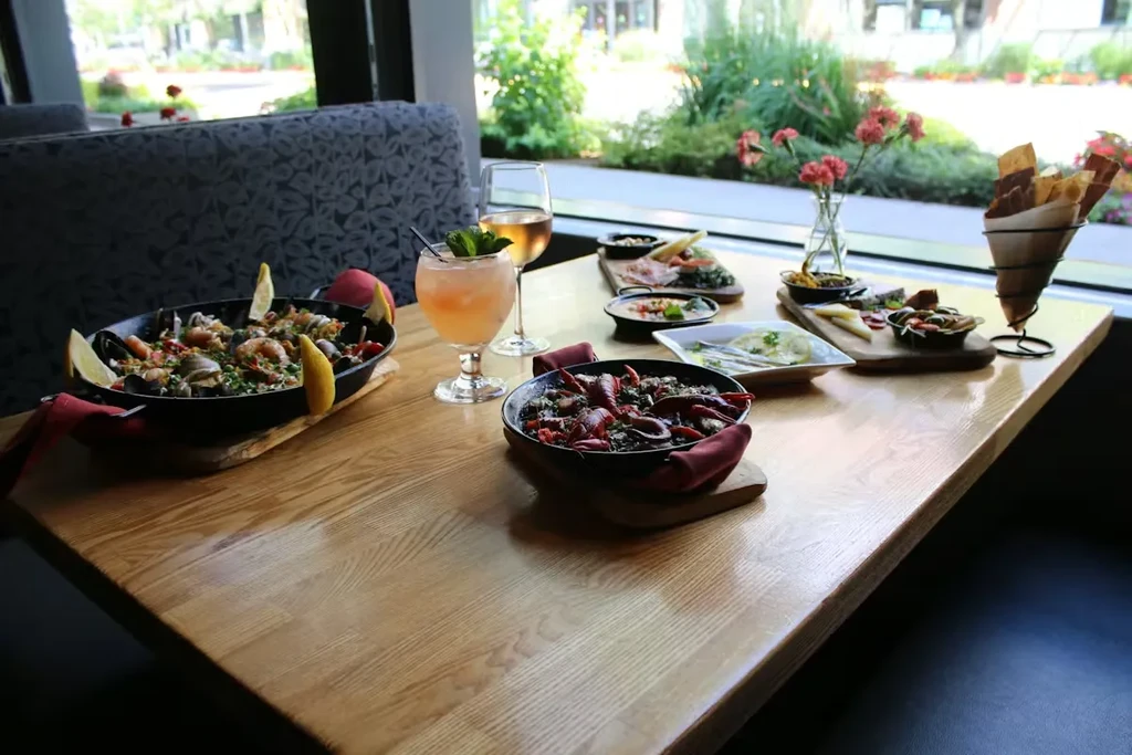 Large seafood paella pans, appetizers, and cocktails on restaurant table.