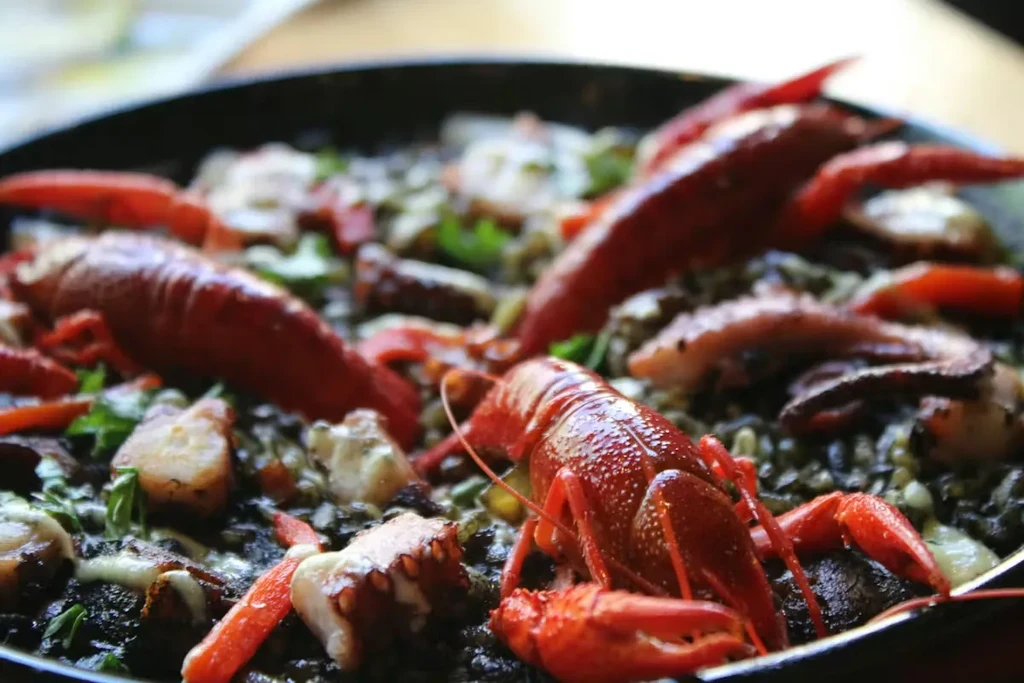 Close-up of black rice paella with red langoustines, octopus, and herbs.
