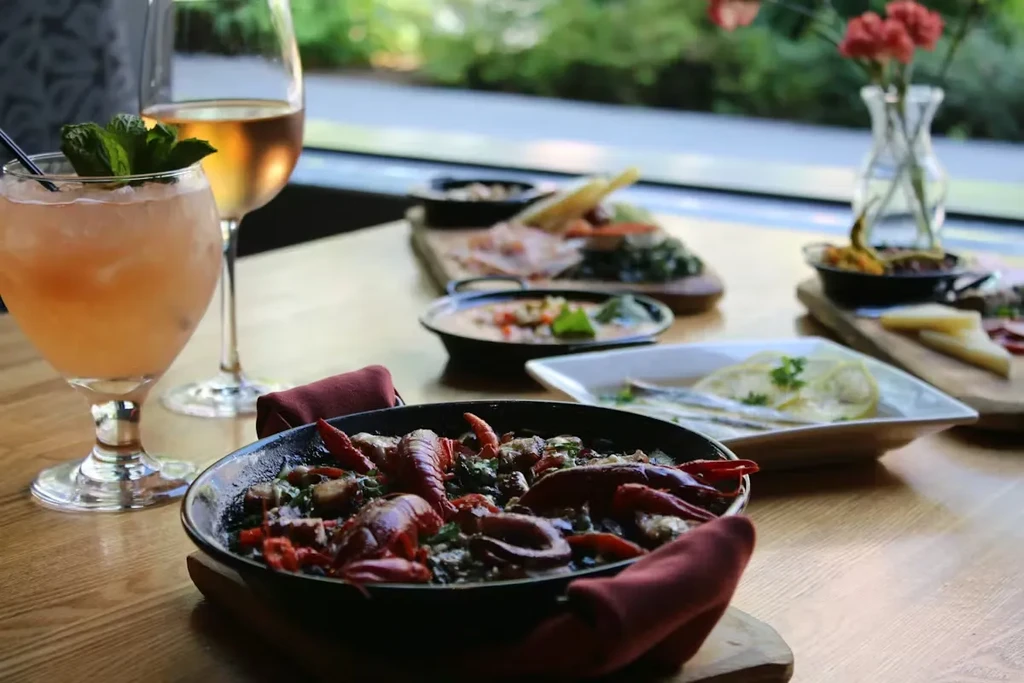 Restaurant table with a skillet of crawfish, cocktails, and appetizers.