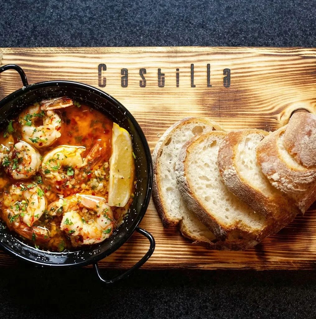 Overhead shot of shrimp in sauce, lemon, and bread on a board.