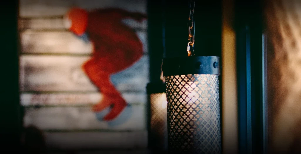 Cylindrical metal mesh lamp glows warmly, blurred stylized figure artwork.