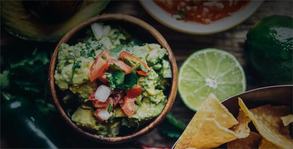 Close-up of guacamole with pico de gallo, tortilla chips, and fresh limes.