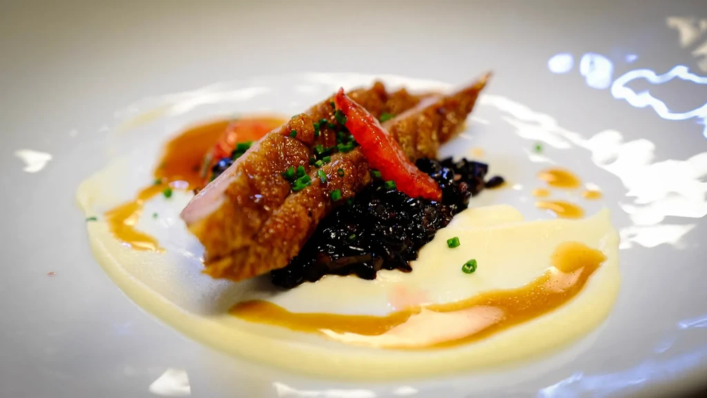 Seared duck breast with black rice, puree, and sauce on a white plate.