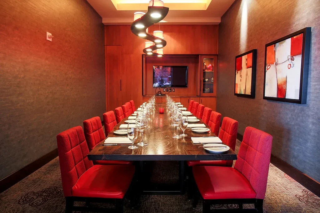 Luxurious private dining room with a long table and red chairs.