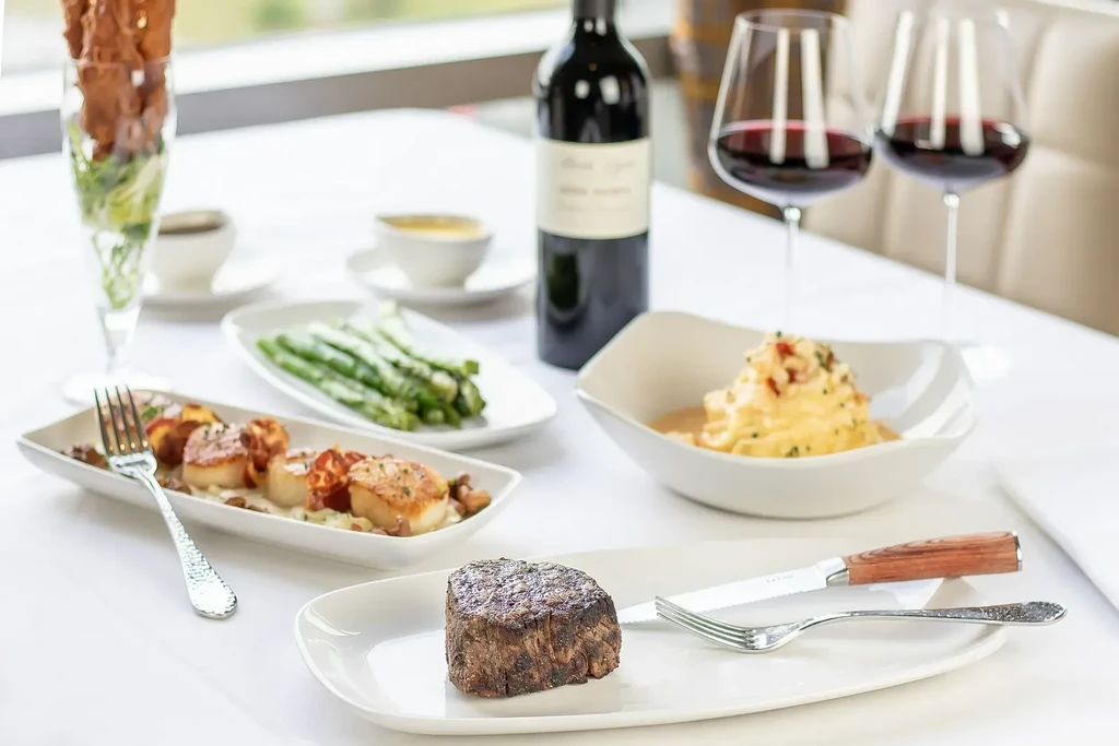 Fine dining table with gourmet dishes: filet mignon, scallops, asparagus, wine.