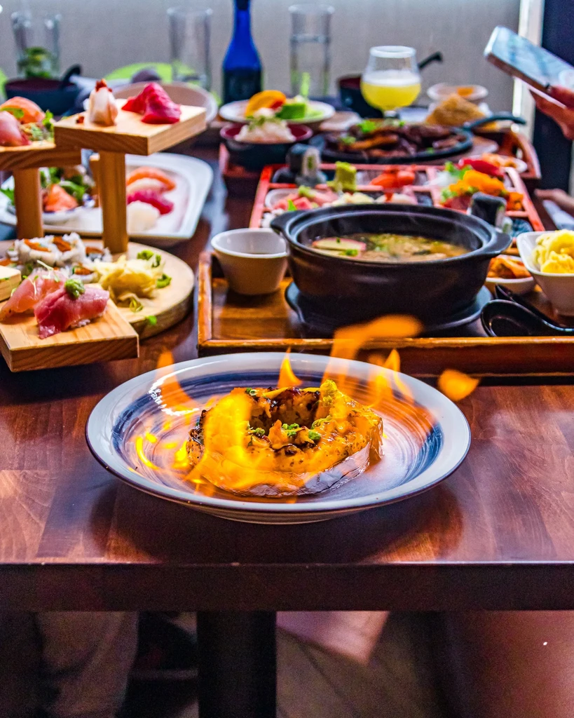 Vibrant Japanese dinner table with flaming squash, sushi, and sake.