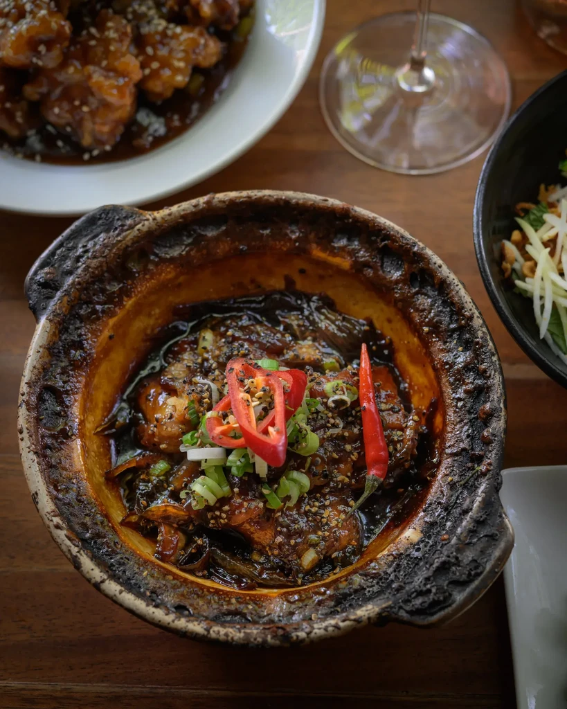 Overhead shot of a dark clay pot dish with chilies and green onions.