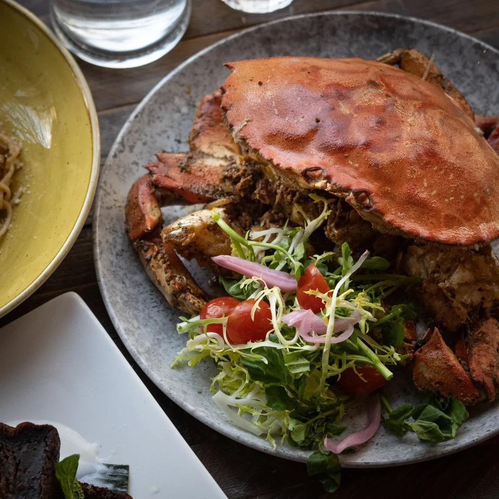 Cooked whole reddish-orange crab and side salad on a grey plate.