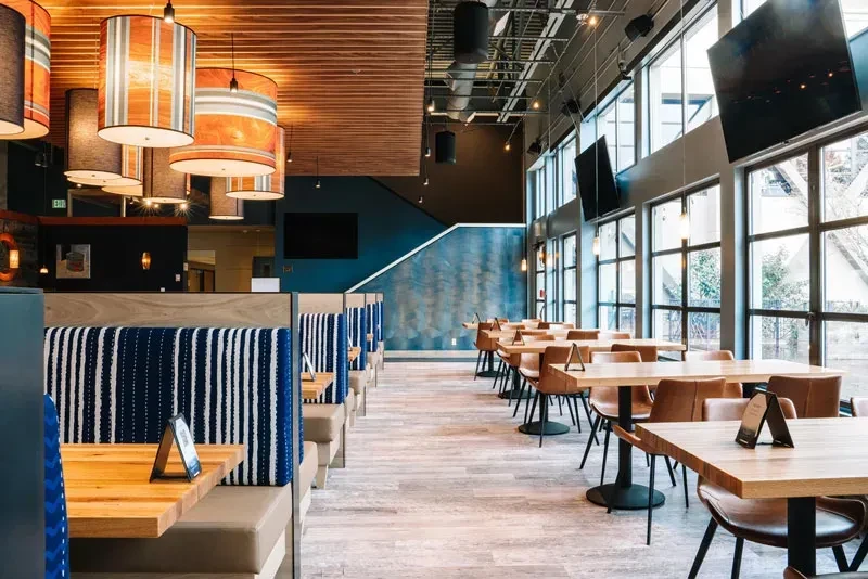 Modern, well-lit restaurant interior with blue booths, tables, and windows.