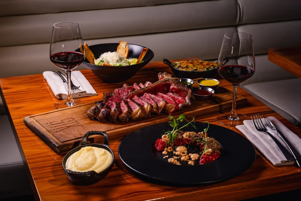 Sliced medium-rare T-bone steak, Caesar salad, and red wine.