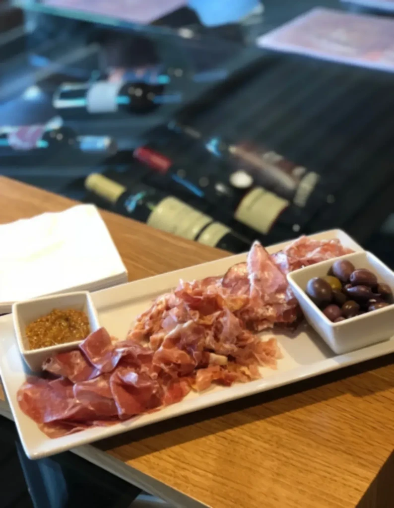Generous plate of cured meats, mustard, and olives on wooden table.