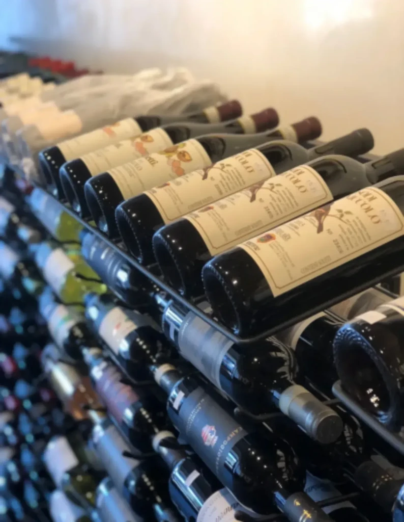 Rows of red wine bottles with light labels on a black rack.