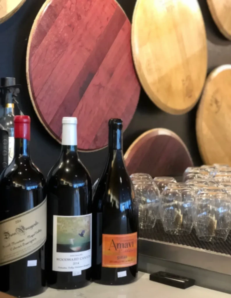 Three wine bottles, stacked glasses, and wooden barrel panels.