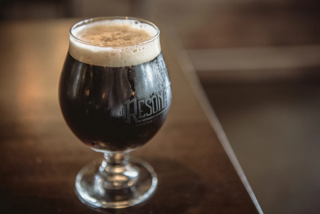 Dark beer in a chilled goblet with a frothy head and brewery logo.