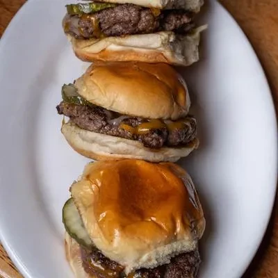 Three stacked beef sliders with melted cheese, pickles, and buns.