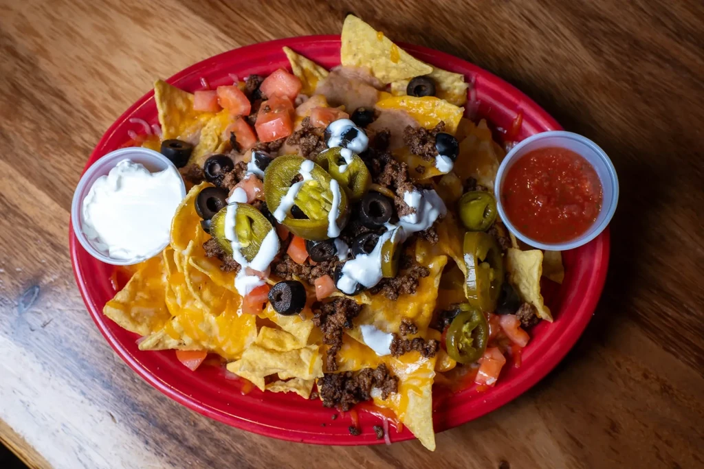 Plate of nachos with beef, cheese, tomatoes, olives, jalapeños, and sauces.