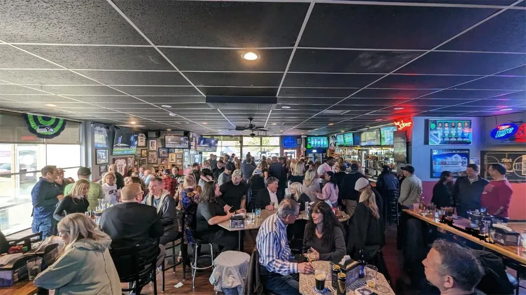 Bustling sports bar interior, many patrons, multiple TVs, and a long bar.