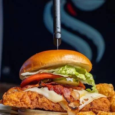 Crispy fried chicken sandwich, bacon, cheese, vegetables, and potato bites.