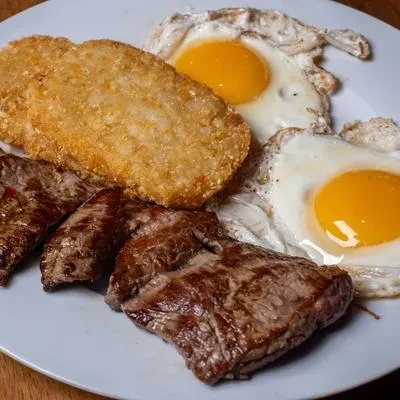 Cooked steak, golden hash brown, and two sunny-side-up eggs.
