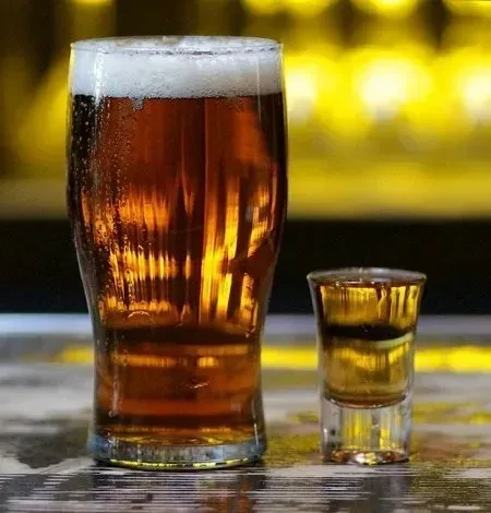 Pint of amber beer and layered shot glass on a bar counter.