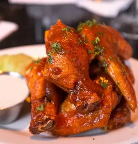 Piled buffalo wings with red sauce, green herbs, and white dip.